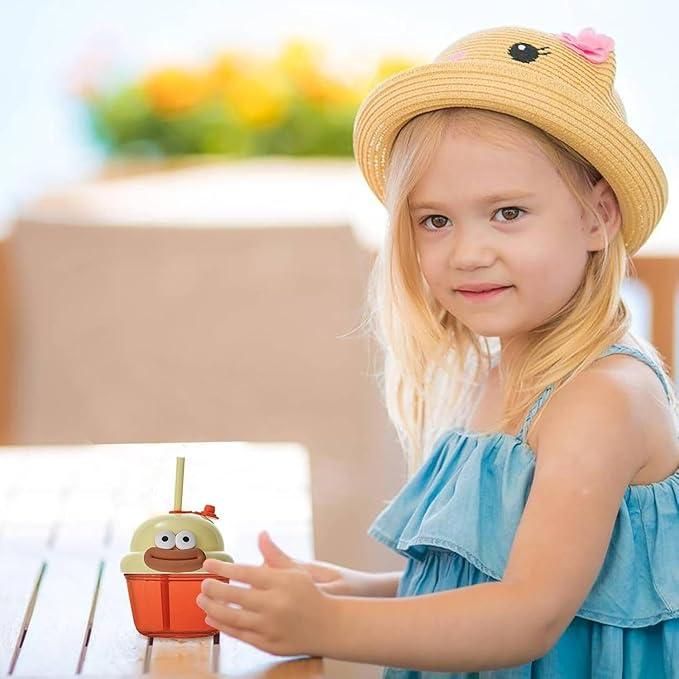 Child using a funny glass cup for children with a playful design and straw on a wooden table