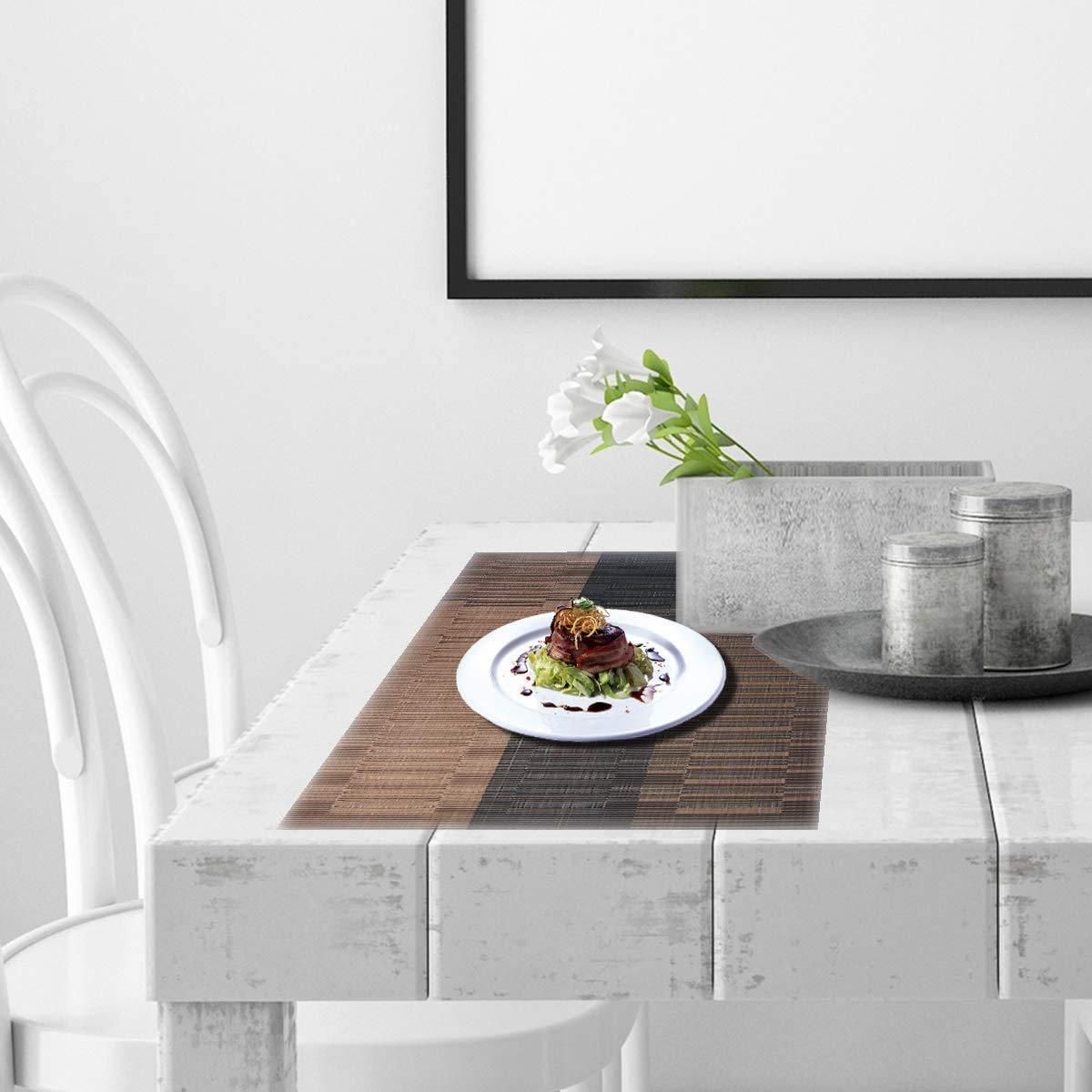 Stylish brown and black placemats on white wooden dining table with floral centerpiece and decorative jars