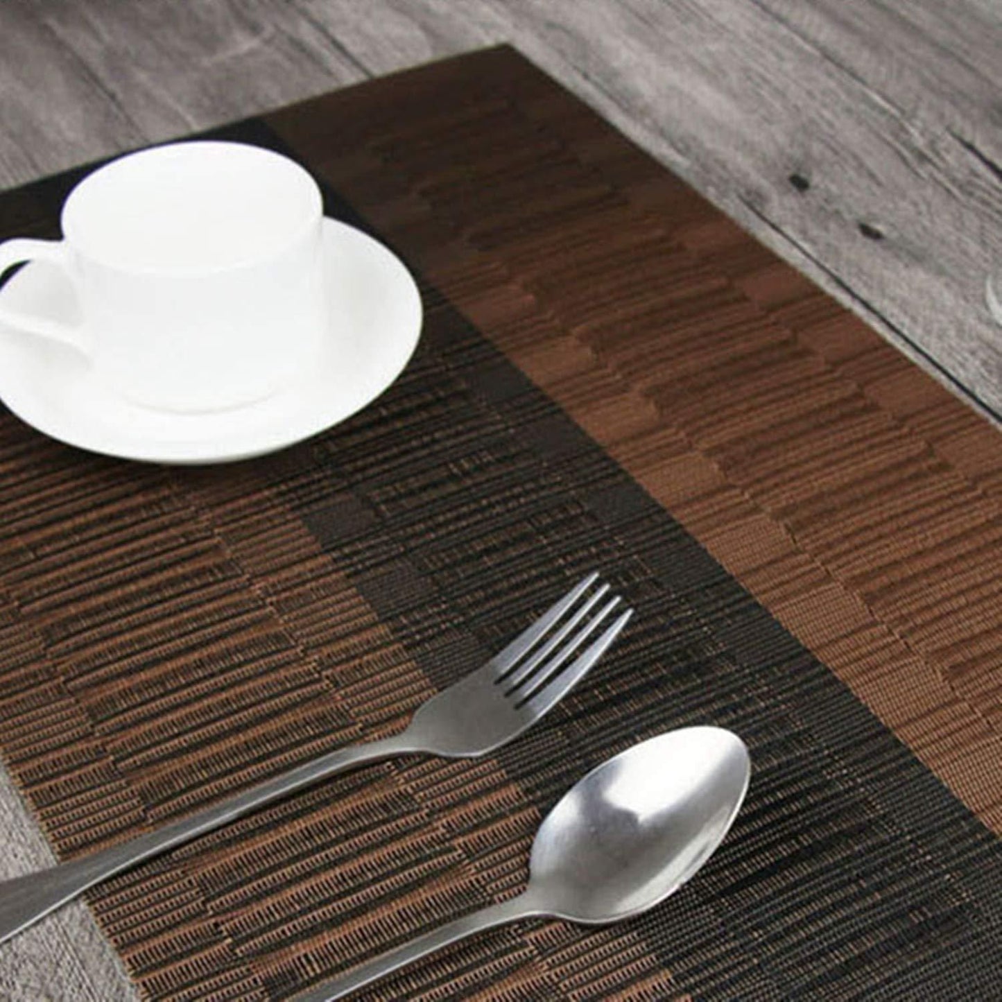 Stylish brown and black placemats with a cup, saucer, fork, and spoon on a wooden table