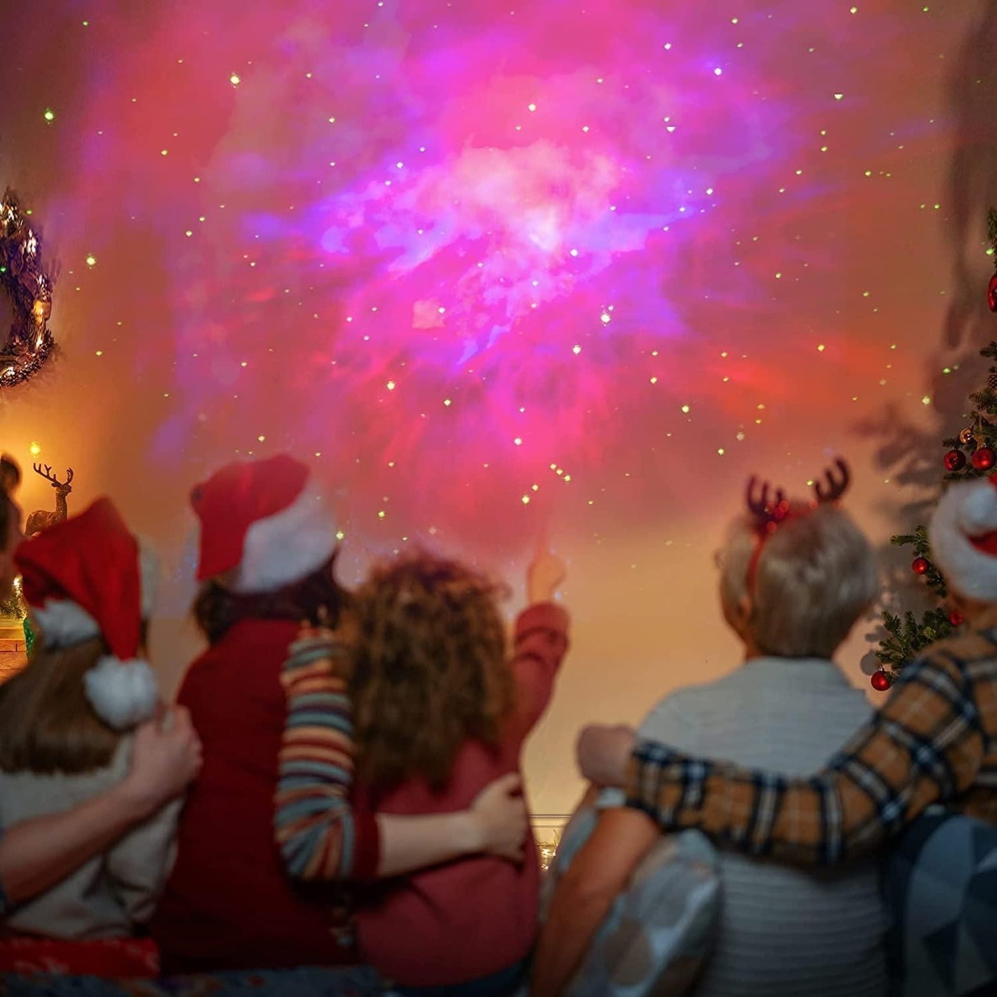 Family wearing Christmas hats enjoying colorful astronaut galaxy projector displaying stars and nebula on wall