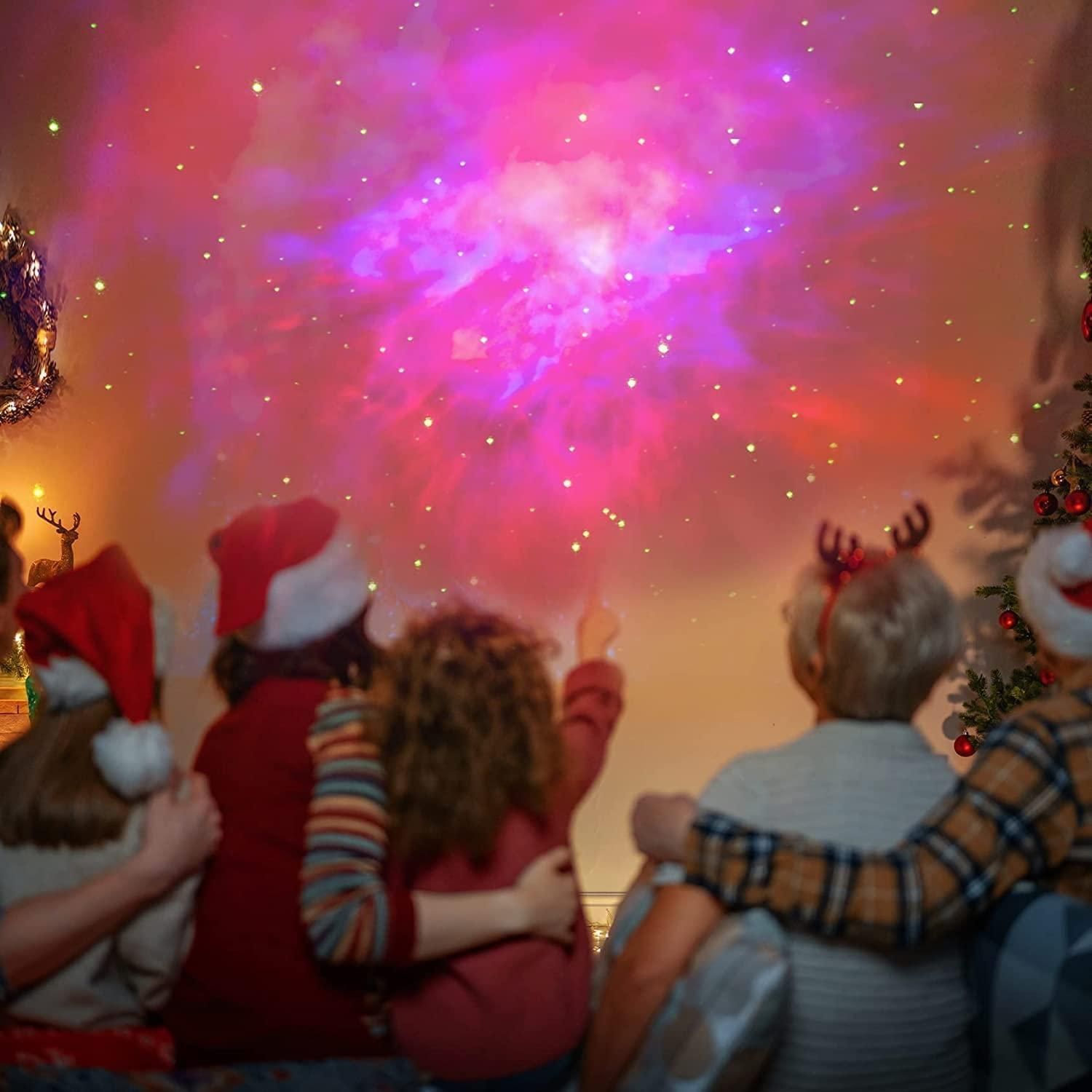 Family wearing Christmas hats enjoying colorful astronaut galaxy projector displaying stars and nebula on wall